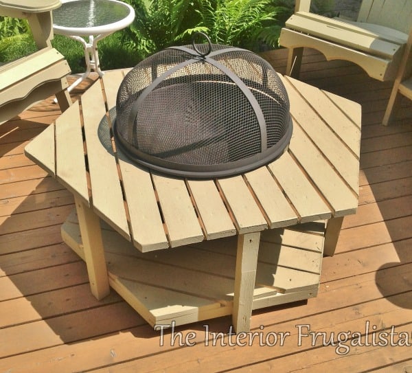 A fire bowl table on the back deck of a house with Adirondack chairs.