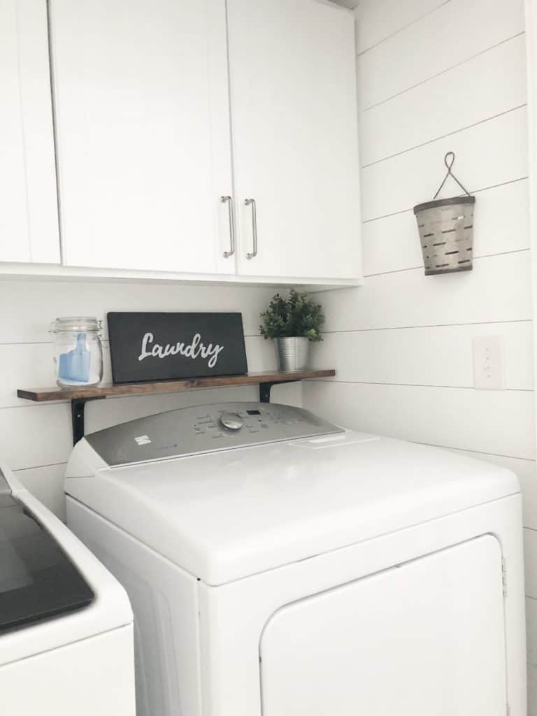 A laundry room with a washer and dryer, white shiplap walls, and white cabinets.