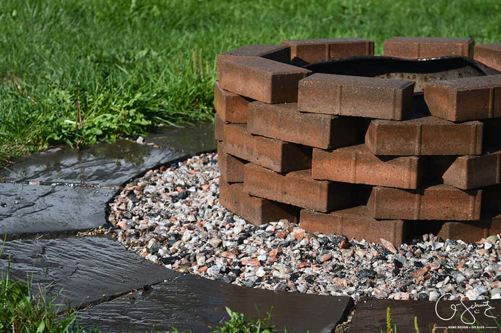 Stacked bricks create a fire pit over gravel in a backyard.