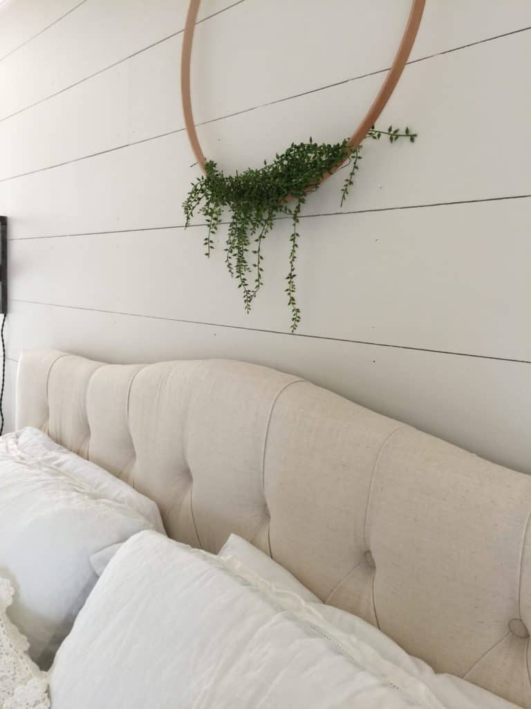 Angled close-up shot of white shiplap walls in a bedroom with a tufted headboard and floral wreath wall hanging.